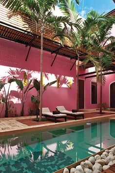 an indoor swimming pool with lounge chairs and palm trees in the background, surrounded by pink walls