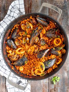 a pan filled with pasta and mussels on top of a wooden table