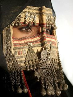 a woman wearing an elaborate headdress with bells and beads on it's face