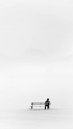 a man sitting on top of a bench in the middle of a foggy field