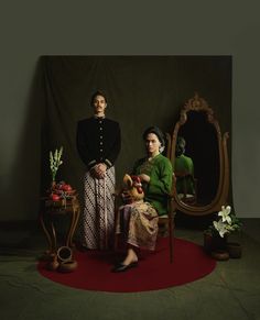 two people are sitting on a red carpet in front of a mirror and table with flowers