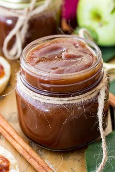 two jars filled with peanut butter sitting on top of a wooden table next to cinnamon sticks