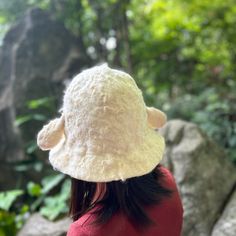 a woman wearing a white hat standing in front of some rocks and trees with her back to the camera