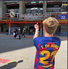 a young boy standing in front of a soccer stadium holding his hand up to the sky