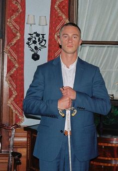 a man wearing a blue suit and tie standing in front of a window with red curtains