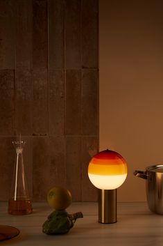 an orange and yellow lamp sitting on top of a counter next to a pot filled with fruit