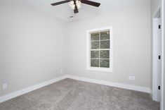 an empty room with a ceiling fan and window in the corner on the far wall