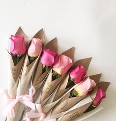 a bunch of pink roses are wrapped in brown paper and tied with ribbon on a white surface