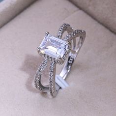 a ring with an emerald cut diamond surrounded by pave diamonds on a cushioned surface