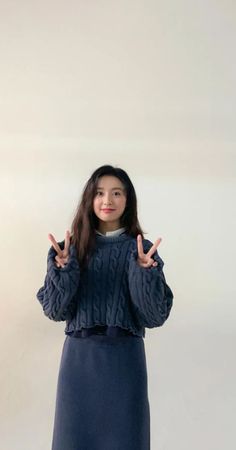 a woman standing in front of a white wall making the peace sign with her hands