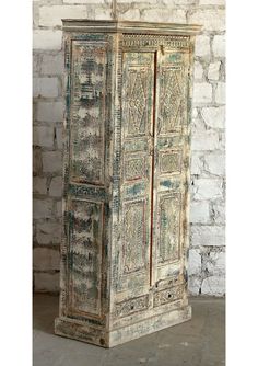 an old wooden cabinet with intricate carvings on the doors and drawers, in front of a brick wall