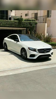 a white mercedes benz coupe parked in front of a building with a garage door open