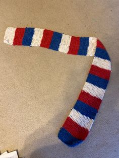 a knitted red, white and blue scarf laying on the floor next to a remote control