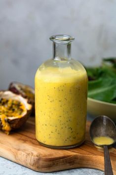 a glass bottle filled with yellow liquid sitting on top of a cutting board next to a bowl and spoon