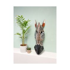 a zebra mask sitting on top of a white shelf next to a potted plant