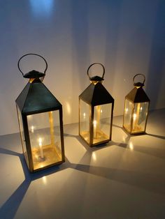 three lit up lanterns sitting next to each other on top of a white countertop