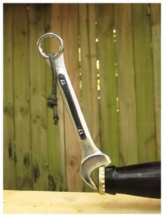 a close up of a wrench on top of a wooden table with a fence in the background