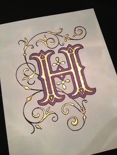 the letter h is made up of gold and purple swirls on a piece of paper