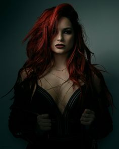 a woman with red hair is posing for a photo in black clothes and necklaces