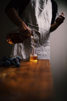 a person pouring something into a glass on top of a wooden table next to grapes