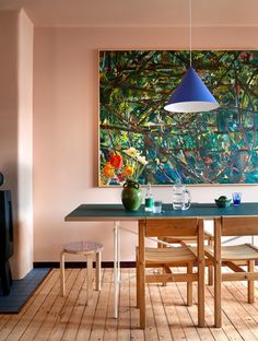 a painting hangs above a dining room table with chairs and a vase on the table