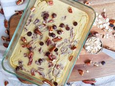 a glass baking dish filled with cake batter and nuts on top of a wooden cutting board