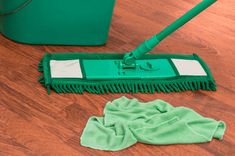 a green mop sitting on top of a wooden floor next to a dust bag