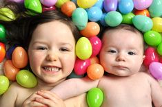 two babies laying next to each other surrounded by colorful balls on the floor and smiling at the camera