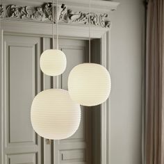 three white paper lanterns hanging from the ceiling in front of an ornate wall and door