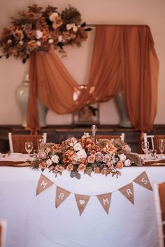 a table is set with flowers and candles for a wedding reception in front of an orange drapes