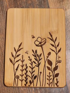 a wooden cutting board with flowers and leaves etched on the side, sitting on a table