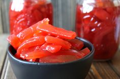 sliced red peppers in a black bowl on a wooden table next to two jars filled with them