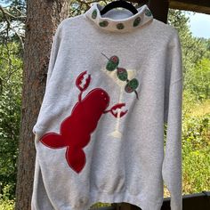 a white sweater with a red lobster on it hanging from a clothes line next to a tree