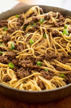 a pan filled with spaghetti and meat on top of a wooden table