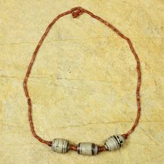 a beaded necklace with red and white beads sits on a stone surface in front of a rock