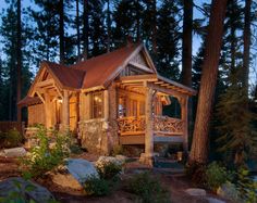 a log cabin in the woods lit up at night with lights shining on it's porch