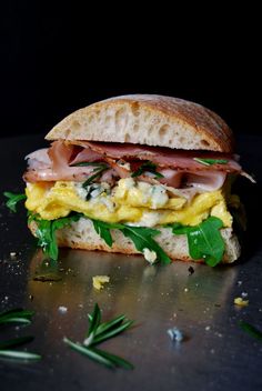 a sandwich with ham, egg and cheese on it sitting on a table next to sprigs of green leaves