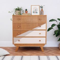 a white and brown dresser sitting on top of a wooden floor next to a potted plant