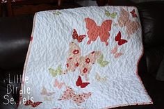 a white quilt with pink and green butterflies on it sitting on a black chair next to a leather couch