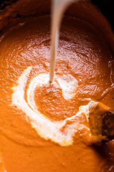 a wooden spoon in a bowl filled with carrots and cream cheese sauce, being stirred by a whisk