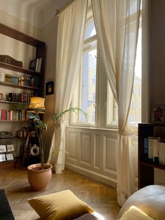 a living room filled with furniture and a window covered in white draping next to a bookshelf