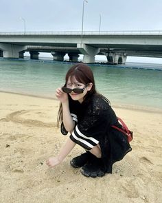 a woman kneeling down on the beach with her hand under her eyeglasses looking at the camera