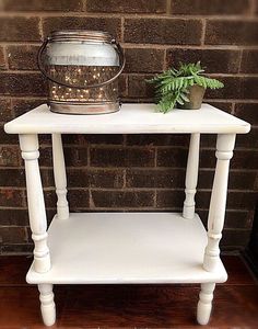 a small white table with a potted plant on it and a metal bucket sitting on top