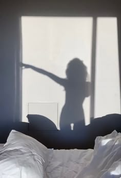 the shadow of a woman standing in front of a bed with white sheets on it