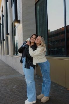 two women standing next to each other in front of a building