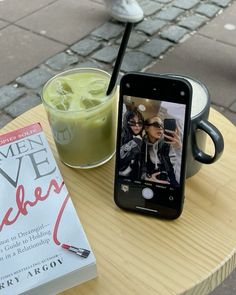 a cell phone sitting on top of a wooden table next to a book and drink