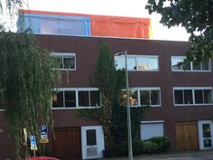 a red car parked in front of a tall brick building with lots of windows and doors