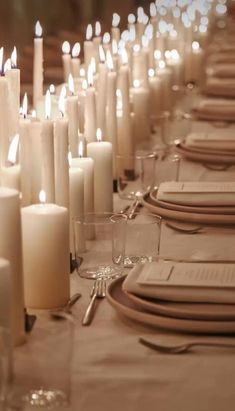 a long table is set with white candles and place settings for dinner guests to enjoy