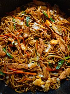 stir fried noodles with chicken and vegetables in a wok on top of a table