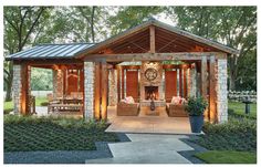 an outdoor living area with stone walls and wood beams, surrounded by grass and trees